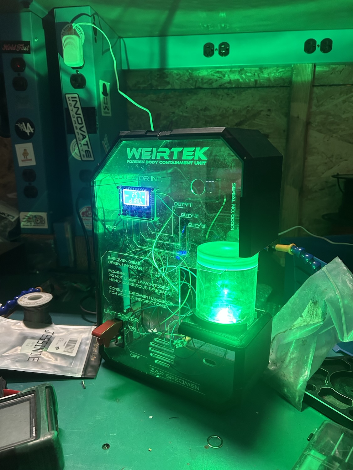 Specimen Lamp powered on, glowing green with exposed circuitry